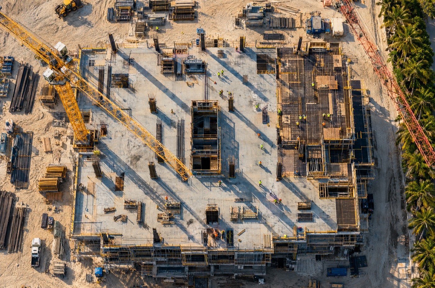 Top-down aerial of a construction site with tower cranes and crews on a concrete deck